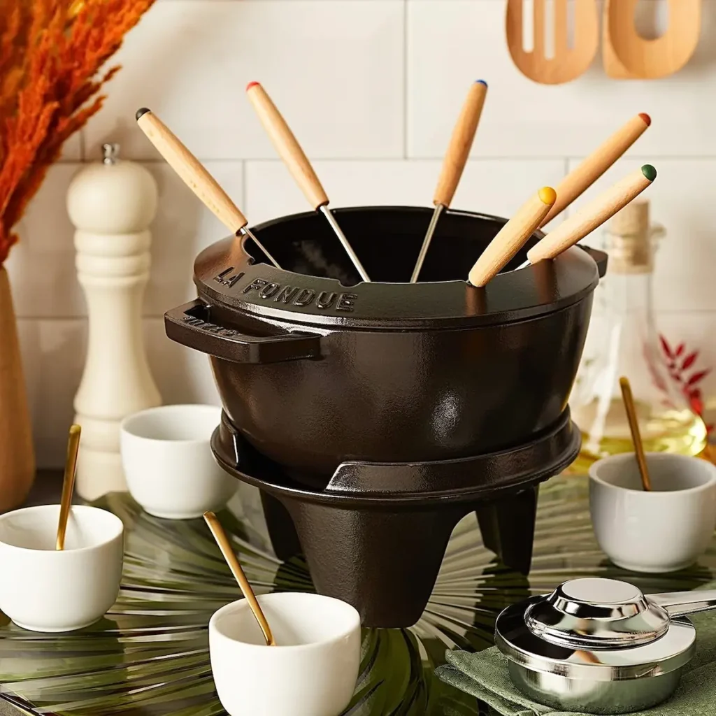 Juego de fondue de hierro fundido negro Staub listo para servir en una cocina decorada con pequeños cuencos de cerámica blanca.