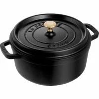 Olla cocotte redonda de hierro fundido negro Staub de 24 cm con asas laterales y pomo dorado sobre fondo blanco.