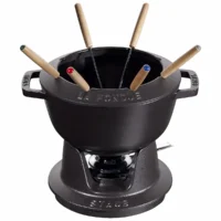 Juego de fondue de hierro fundido negro Staub de 20 cm con base de rechaud, quemador y seis tenedores sobre fondo blanco.