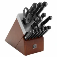 Juego de cuchillos Henckels Solution de 14 piezas con mangos negros de triple remache y tijeras de cocina alojados en un bloque autoafilable de madera sobre fondo blanco.